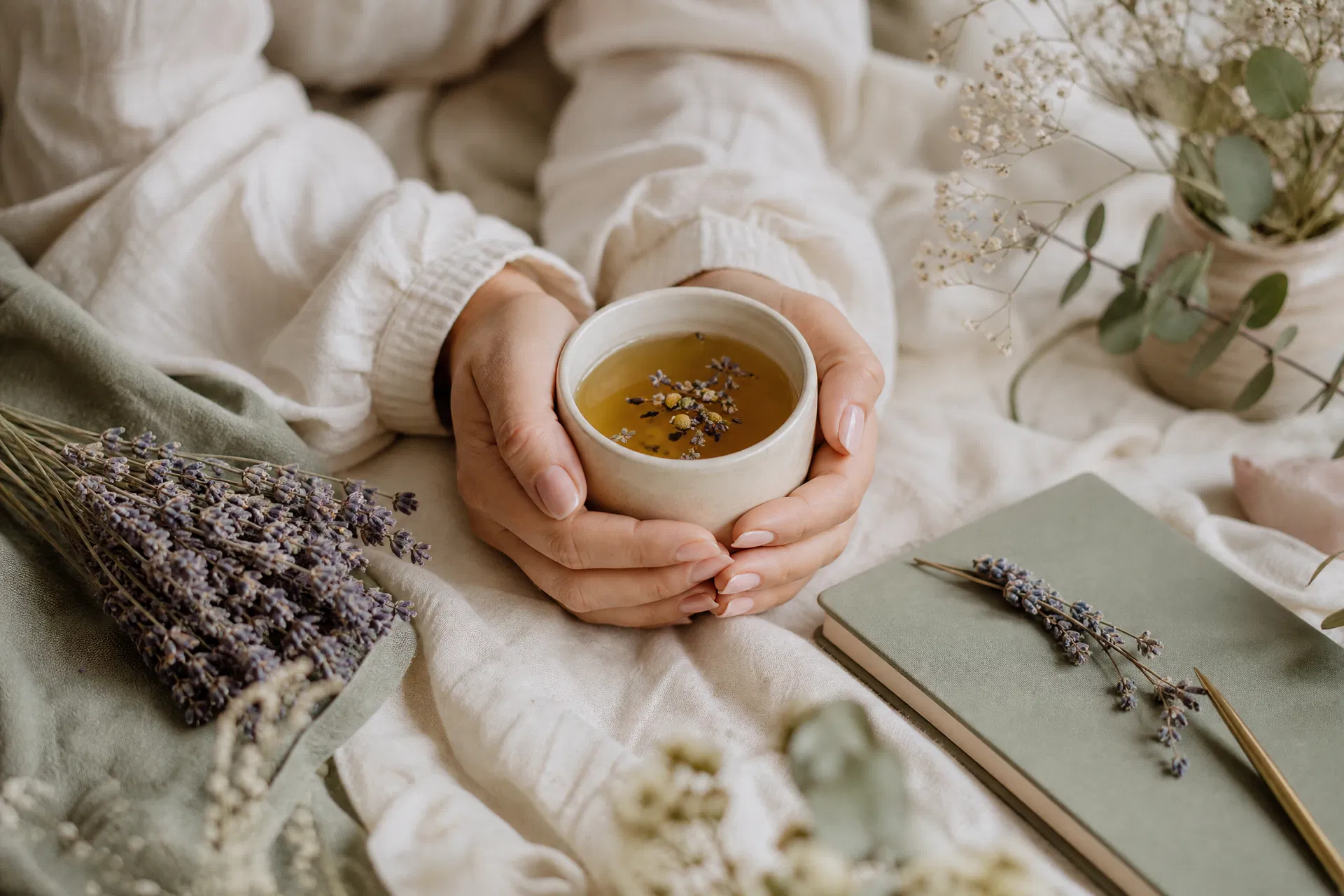 Hands cradling a warm mug of herbal tea surrounded by dried lavender and a journal, PMDD hormonal health nervous system